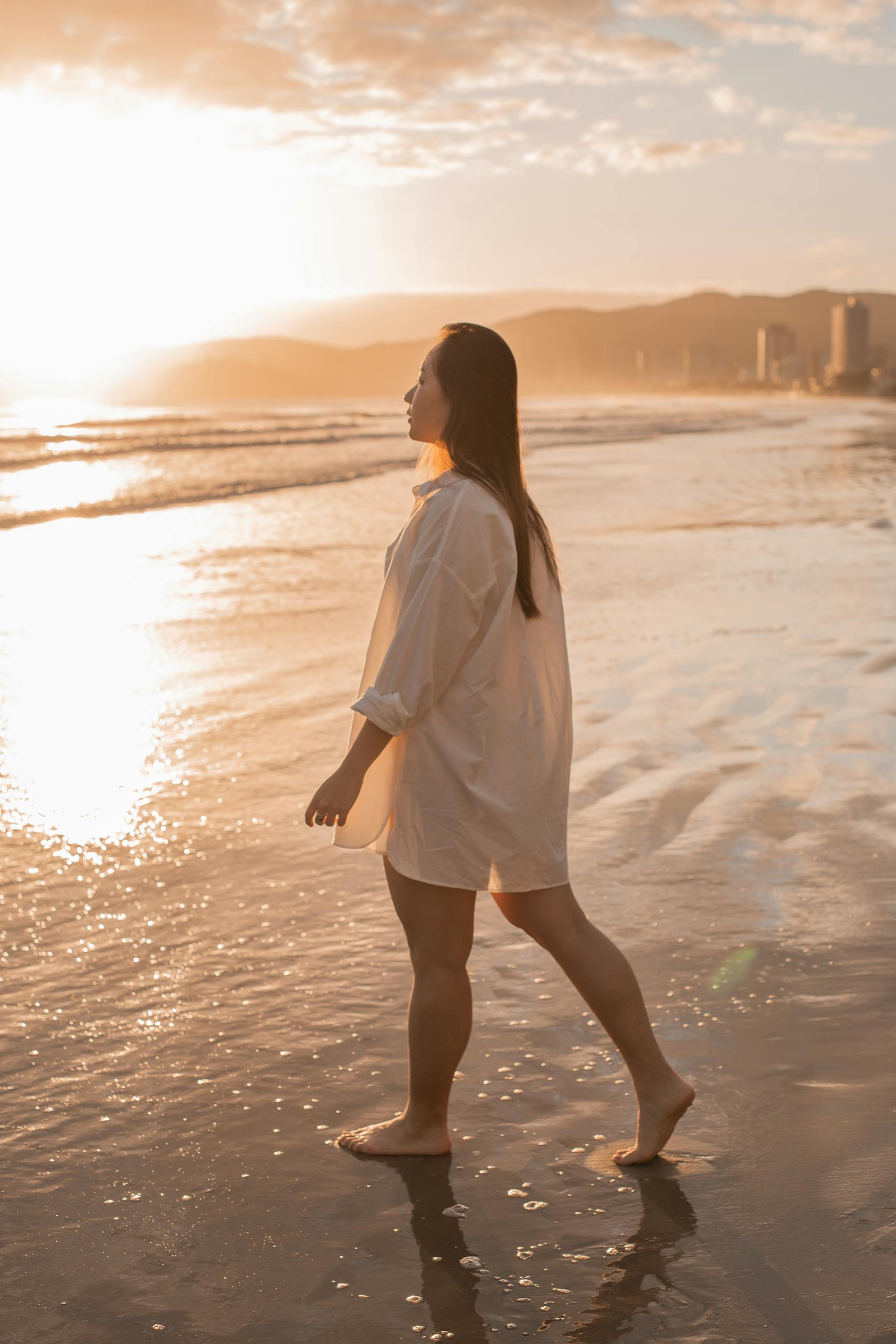 Woman walking barefoot on the beach at sunset, enjoying a tranquil summer evening.